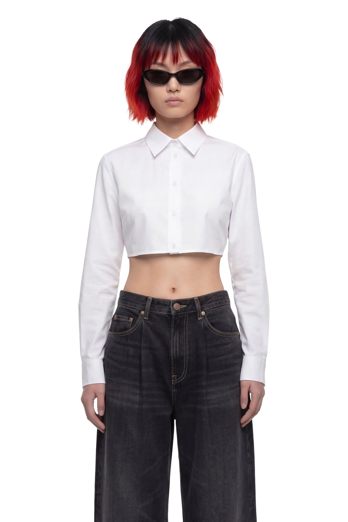 A model with short red and black hair wearing a white long-sleeve cropped button-up shirt and dark wide-leg jeans, photographed against a solid white background.