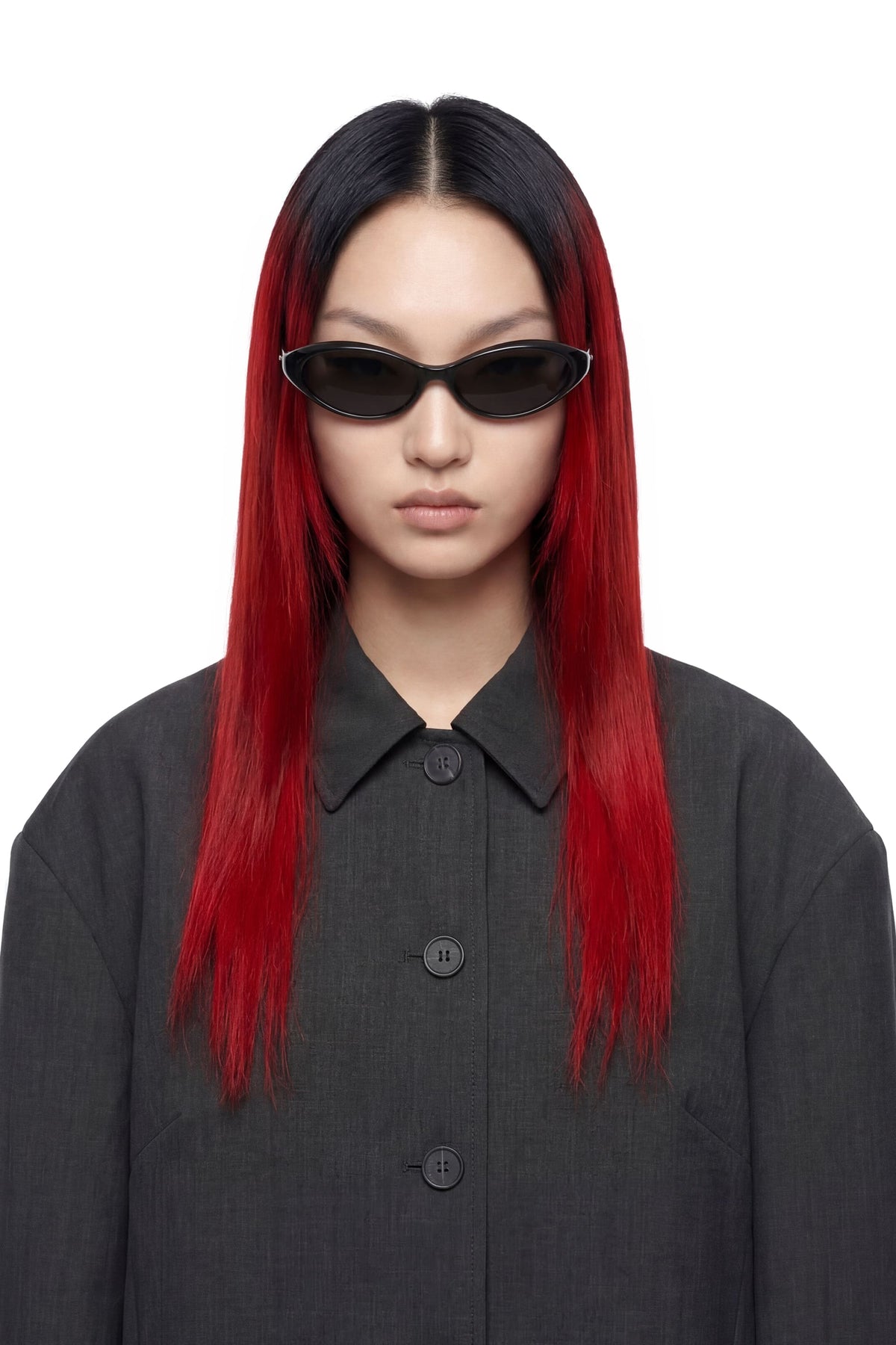 A model with long, straight black hair featuring vibrant red ombre ends, wearing black cat-eye sunglasses and a dark gray button-up shirt against a plain white background.