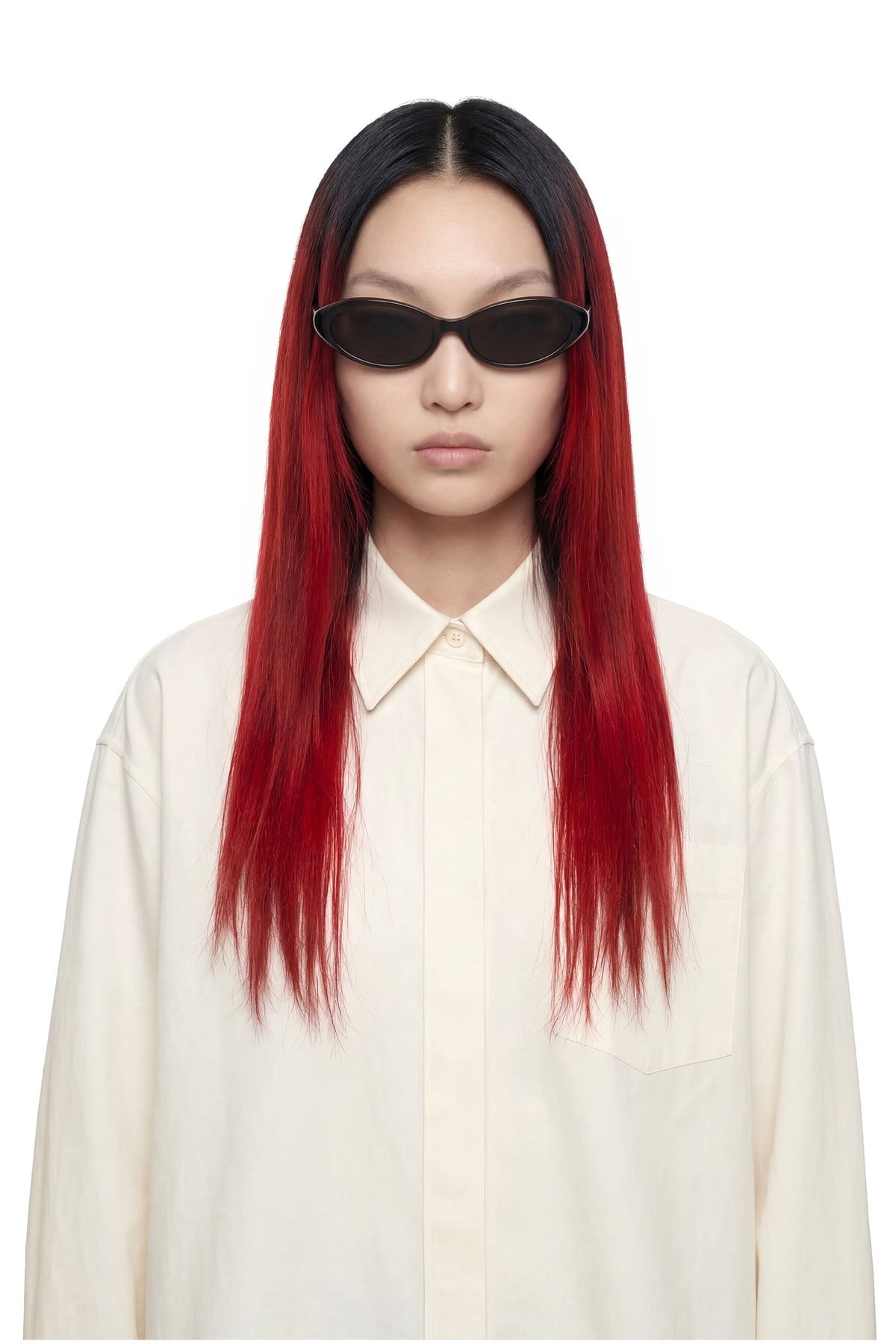 A model with long, straight black-to-red ombre hair wearing a cream button-up shirt and black sunglasses, photographed against a solid white background.
