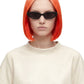A model with a vibrant orange-to-blonde ombre bob haircut wearing black cat-eye sunglasses and a cream-colored oversized t-shirt, set against a plain white background.