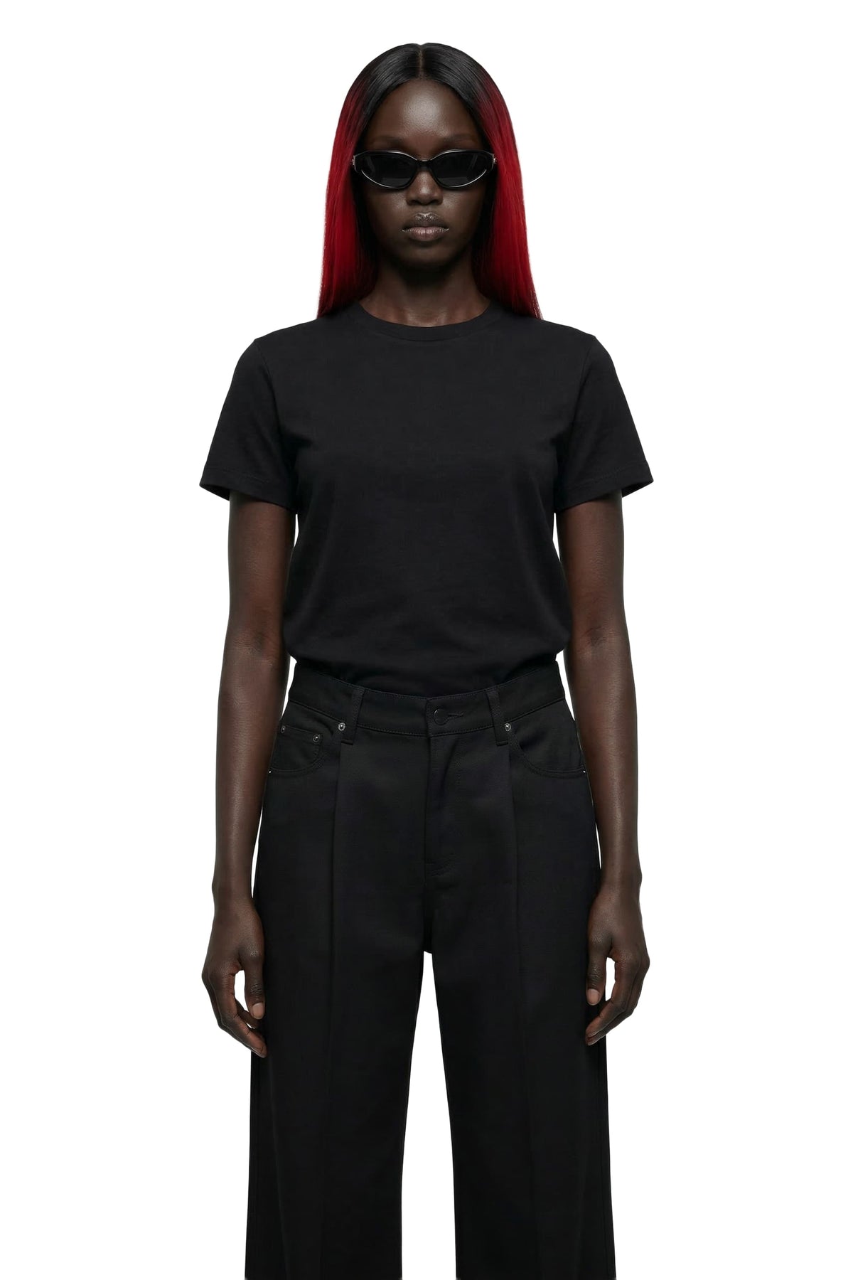 A model with long black hair and vibrant red streaks wears a plain black short-sleeve crewneck t-shirt and black wide-leg trousers, styled with black sunglasses, against a solid white background.