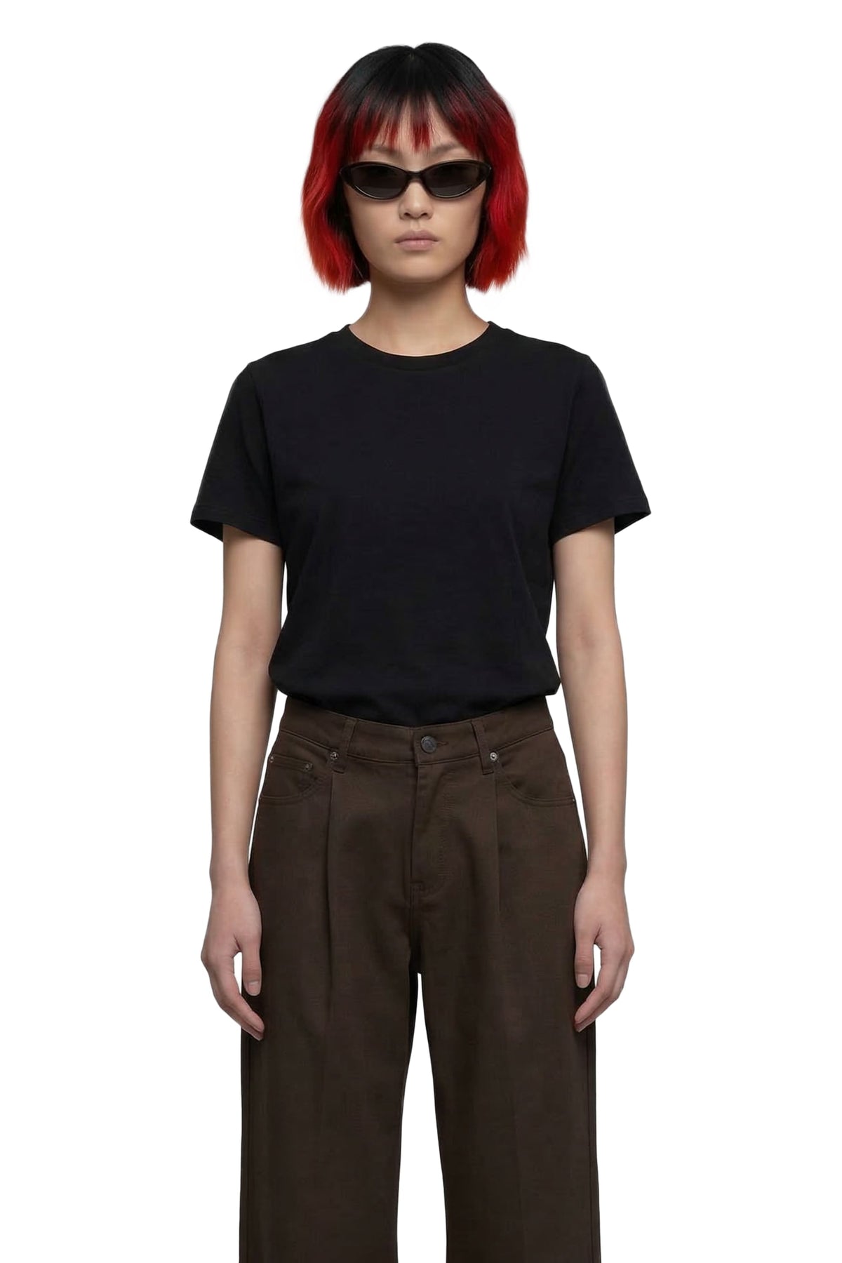 A model with a red and black bob haircut wearing a plain black short-sleeve crewneck t-shirt and dark brown wide-leg trousers, styled with black sunglasses, against a solid white background.