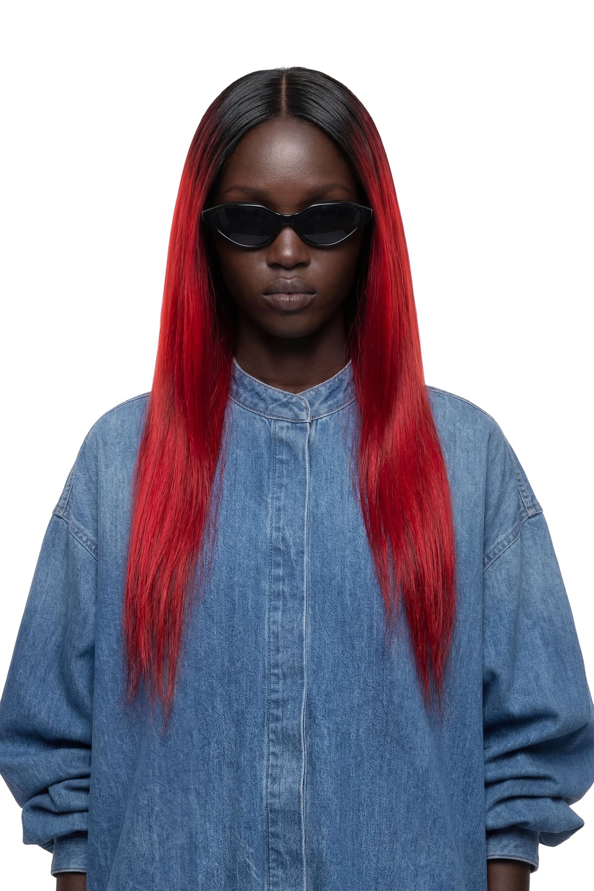 A model with long, straight black hair featuring vibrant red ombre ends, wearing a blue denim shirt and black sunglasses against a solid white background.