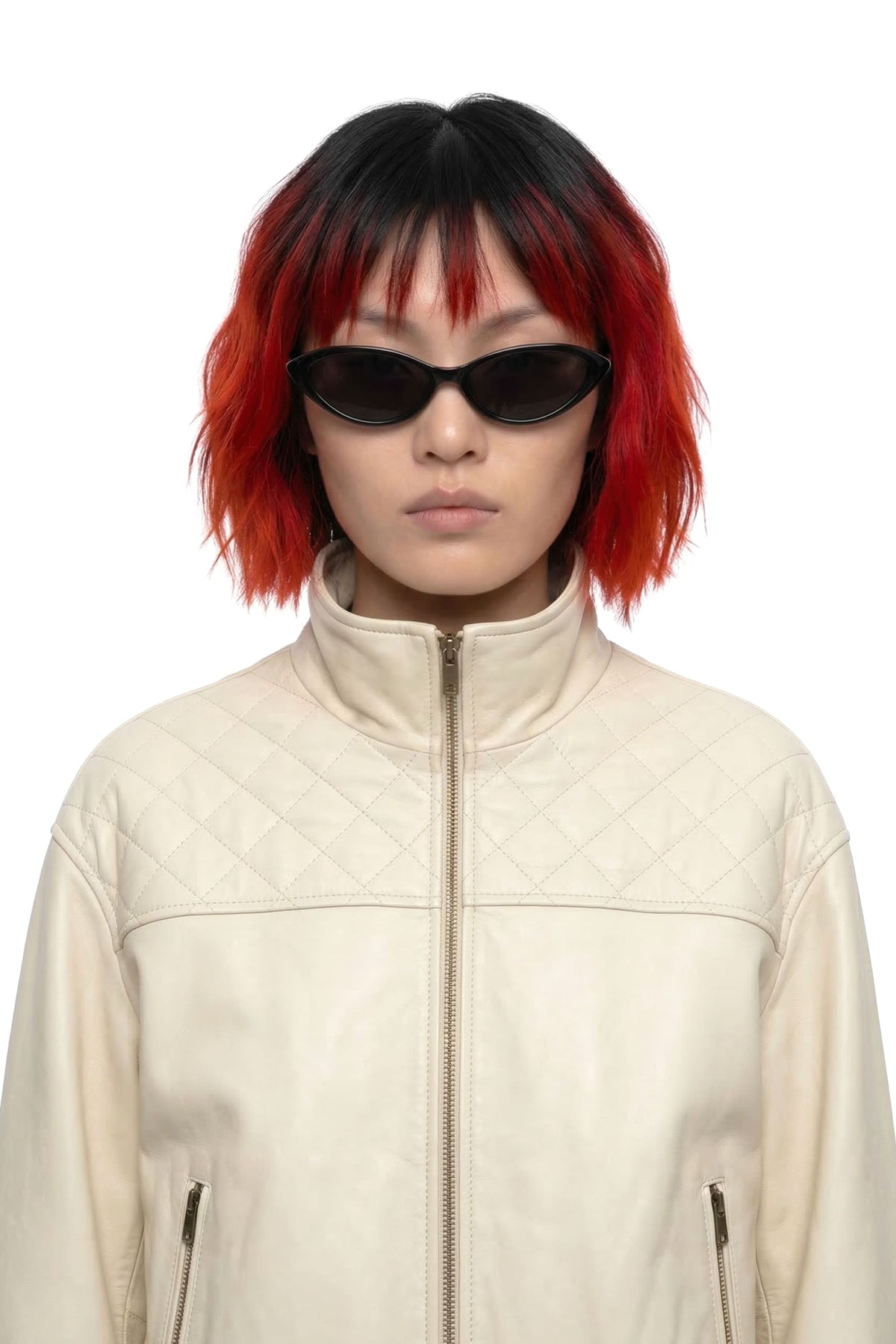 A model with a black and red ombre bob haircut wearing black cat-eye sunglasses and a cream quilted leather jacket, photographed against a solid white background.