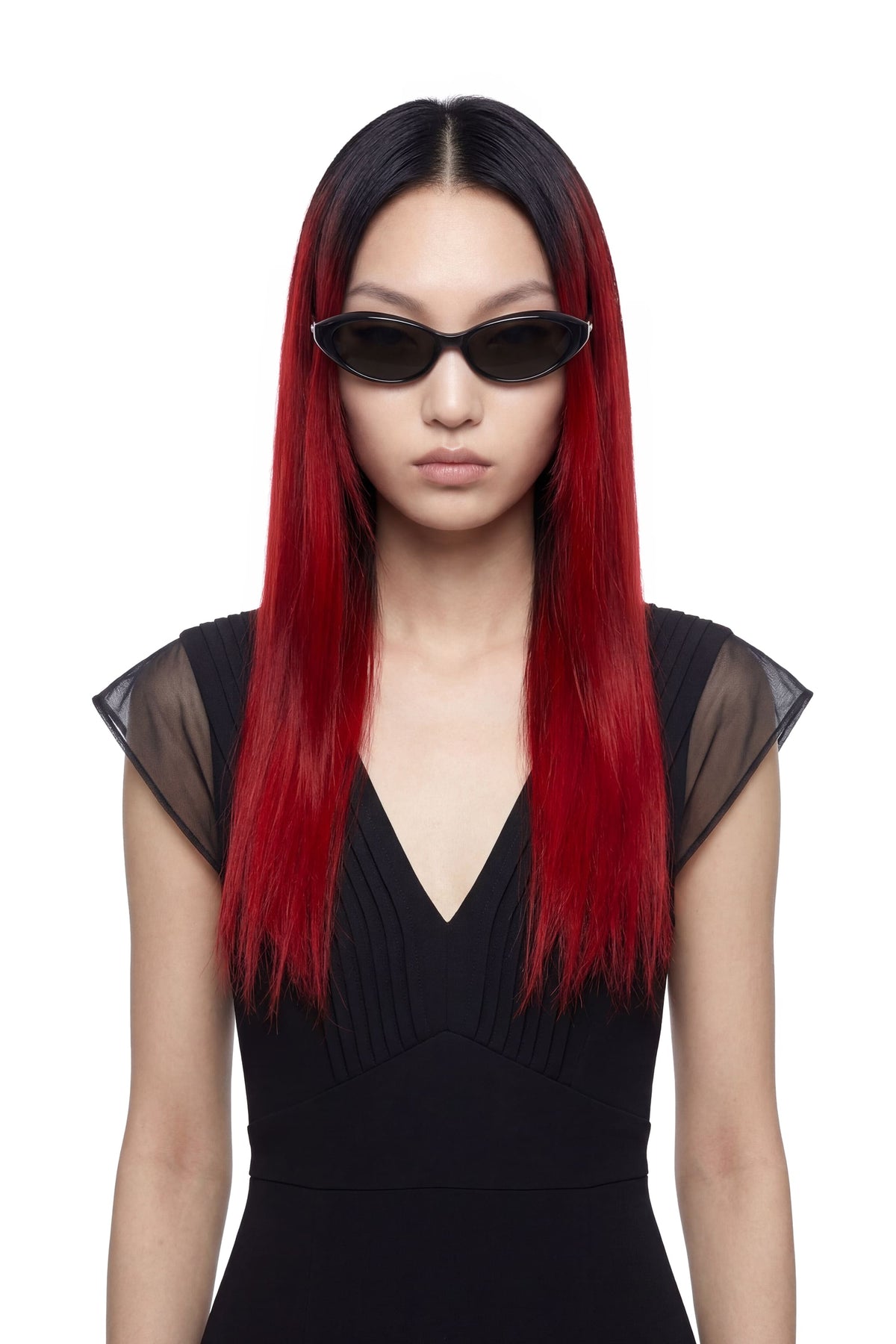A model with long, straight black hair featuring vibrant red ombre ends, wearing black cat-eye sunglasses and a black dress against a plain white background.