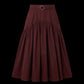 A dark burgundy pleated midi skirt with a matching waistband belt and silver-tone ring buckle, shown against a solid black background.