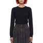A model with short red and black hair wearing a black long-sleeve crewneck top and a dark gray pleated denim skirt, standing against a plain white background.