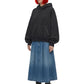 A model with bright orange hair wearing a black oversized hoodie, a blue denim midi skirt, and black combat boots, photographed against a solid white background.