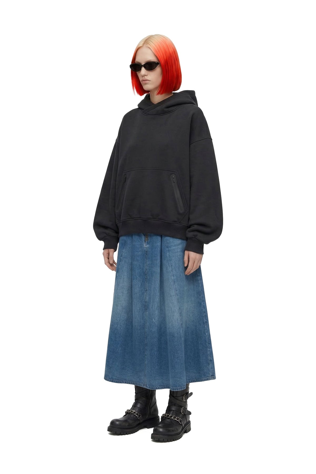 A model with bright orange hair wearing a black oversized hoodie, a blue denim midi skirt, and black combat boots, photographed against a solid white background.