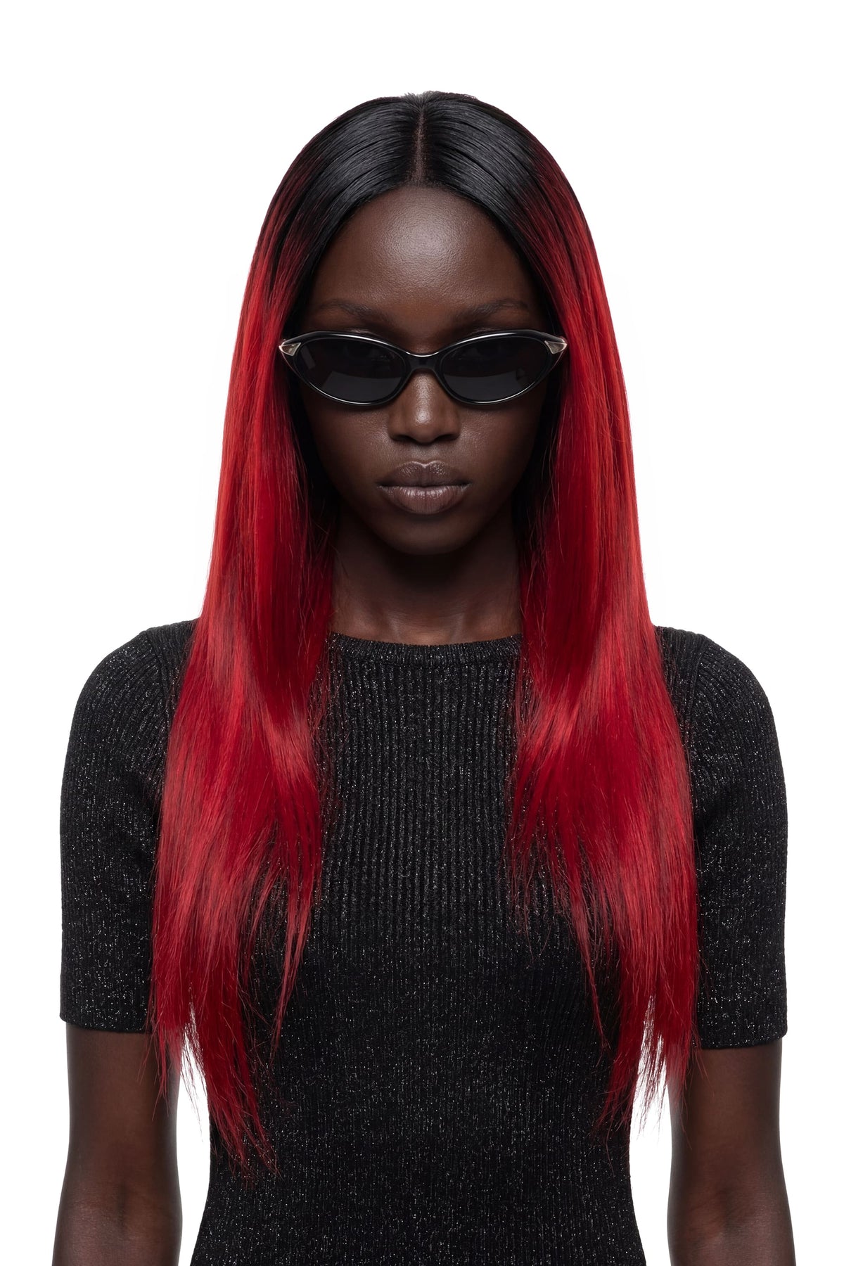 A model with long, straight black hair featuring vibrant red ombre ends, wearing black sunglasses and a black ribbed knit top against a solid white background.