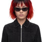 A model with a short black and vibrant red ombre wig wearing black cat-eye sunglasses and a black suede jacket, photographed against a solid white background.