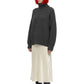 A model with a bright orange-red bob haircut and black sunglasses is shown wearing a dark gray textured knit turtleneck sweater, a cream satin midi skirt, and black pointed-toe boots against a plain white background.