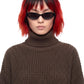 A model with a black and red ombre wig wearing a brown waffle-knit turtleneck sweater and black sunglasses, photographed against a solid white background.