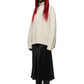 A model with long red hair wearing a cream-colored textured knit turtleneck sweater, a black midi skirt, and black pointed-toe boots, standing against a solid white background.