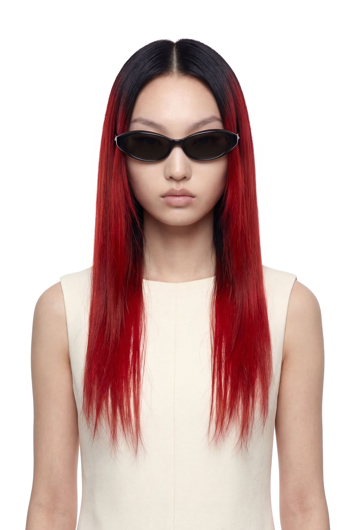 A model with long, straight black-to-red ombre hair wearing black cat-eye sunglasses and a cream-colored sleeveless top, set against a plain white background.