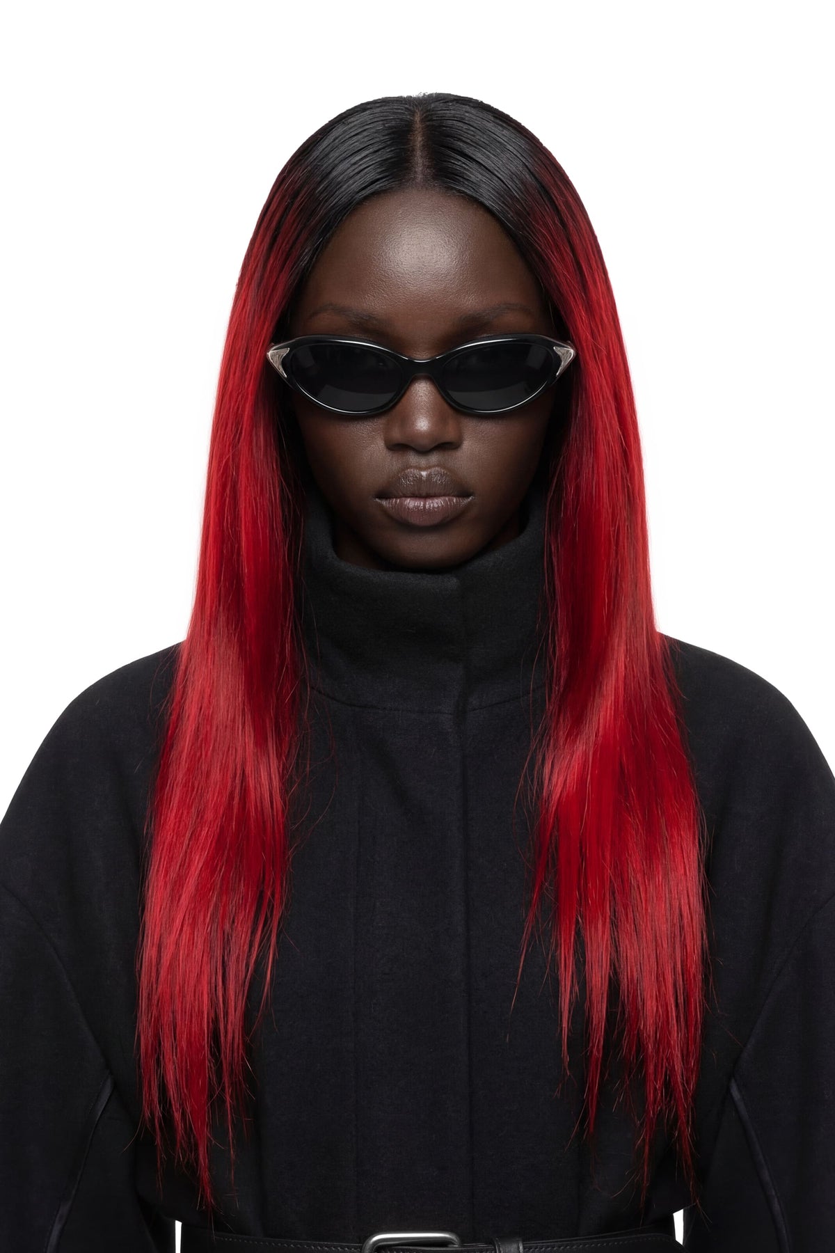 A model with long, straight black hair featuring vibrant red ombré ends, wearing black cat-eye sunglasses and a black turtleneck top against a solid white background.