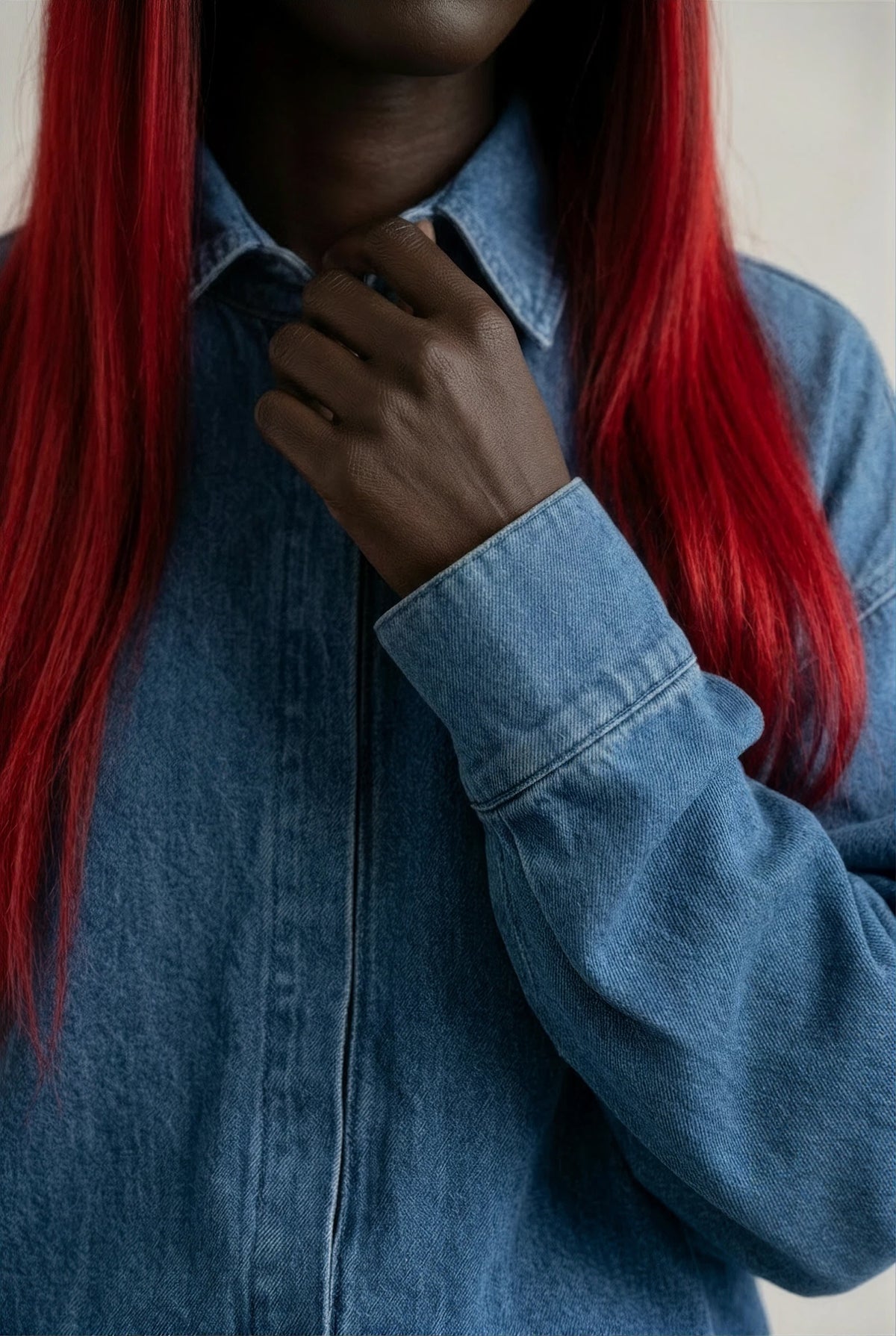 A close-up of a person wearing a blue denim button-up shirt, with long bright red hair visible against a plain light background.