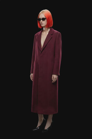 A long burgundy wool-blend coat with notch lapels, front closure, and side pockets, shown against a solid black background.