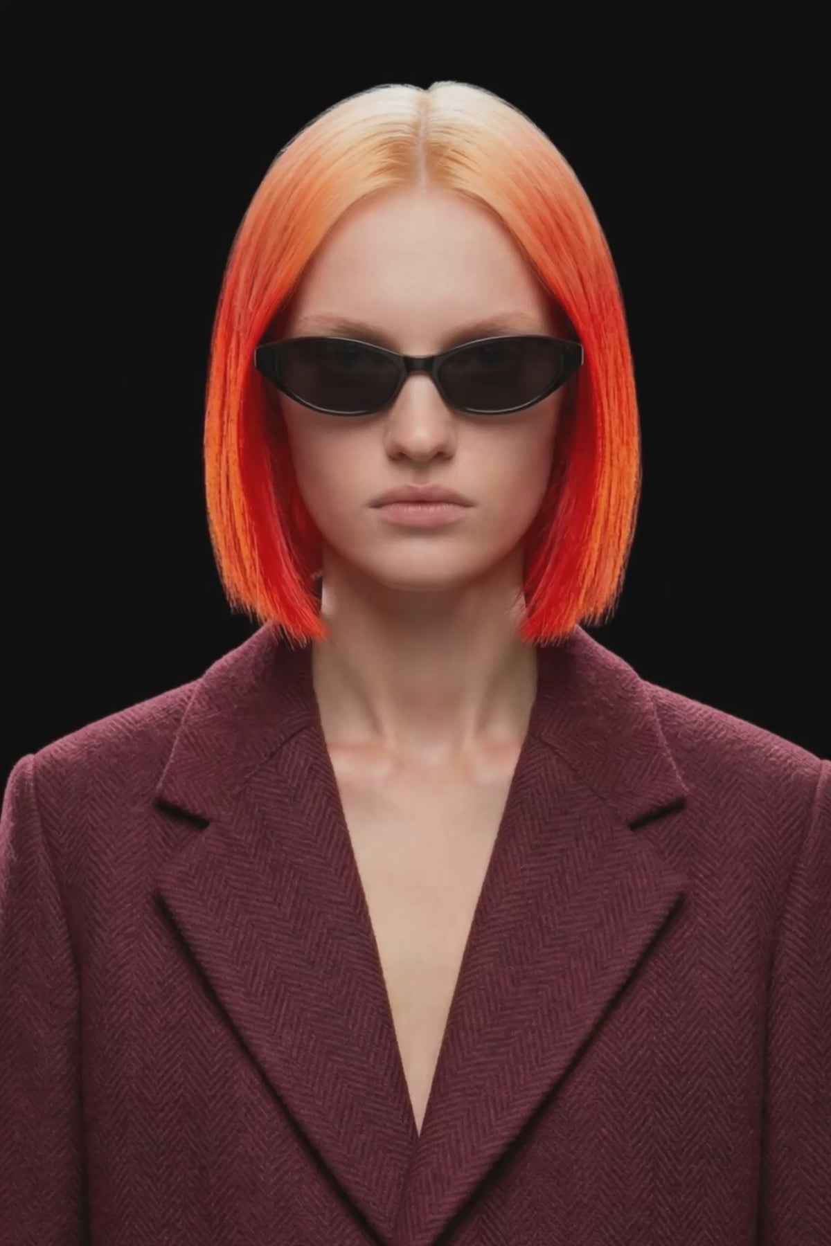 A long burgundy wool-blend coat with notch lapels, front closure, and side pockets, shown against a solid black background.