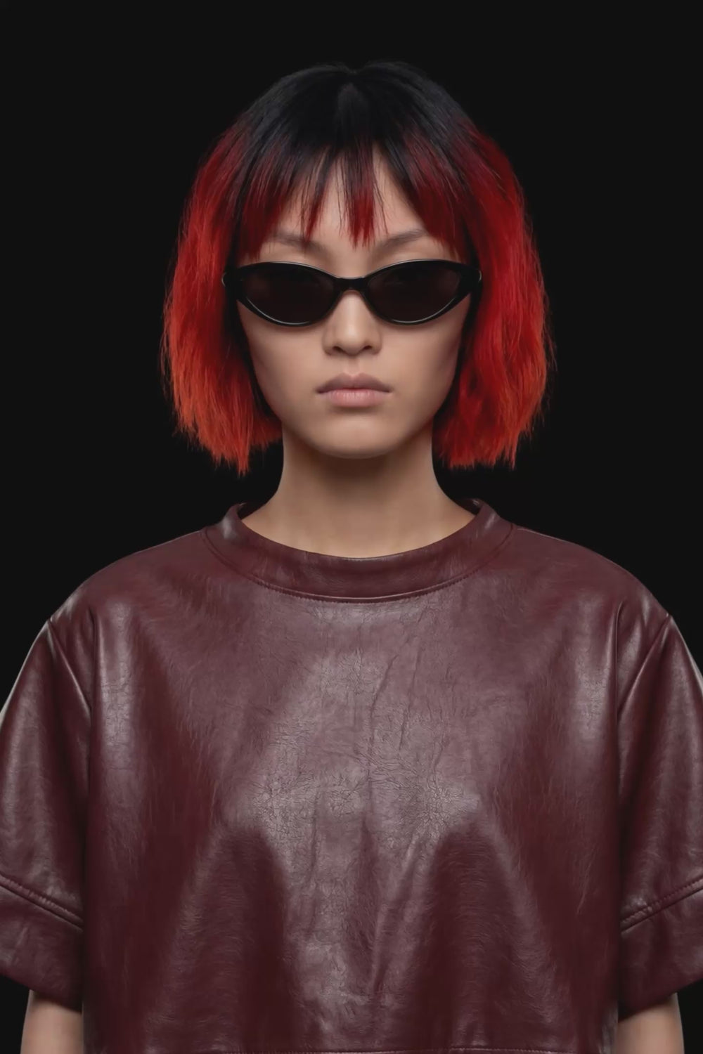 A short-sleeve cropped faux-leather top in a deep burgundy color, featuring a layered asymmetrical hem, displayed against a solid black background.