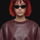 A short-sleeve cropped faux-leather top in a deep burgundy color, featuring a layered asymmetrical hem, displayed against a solid black background.