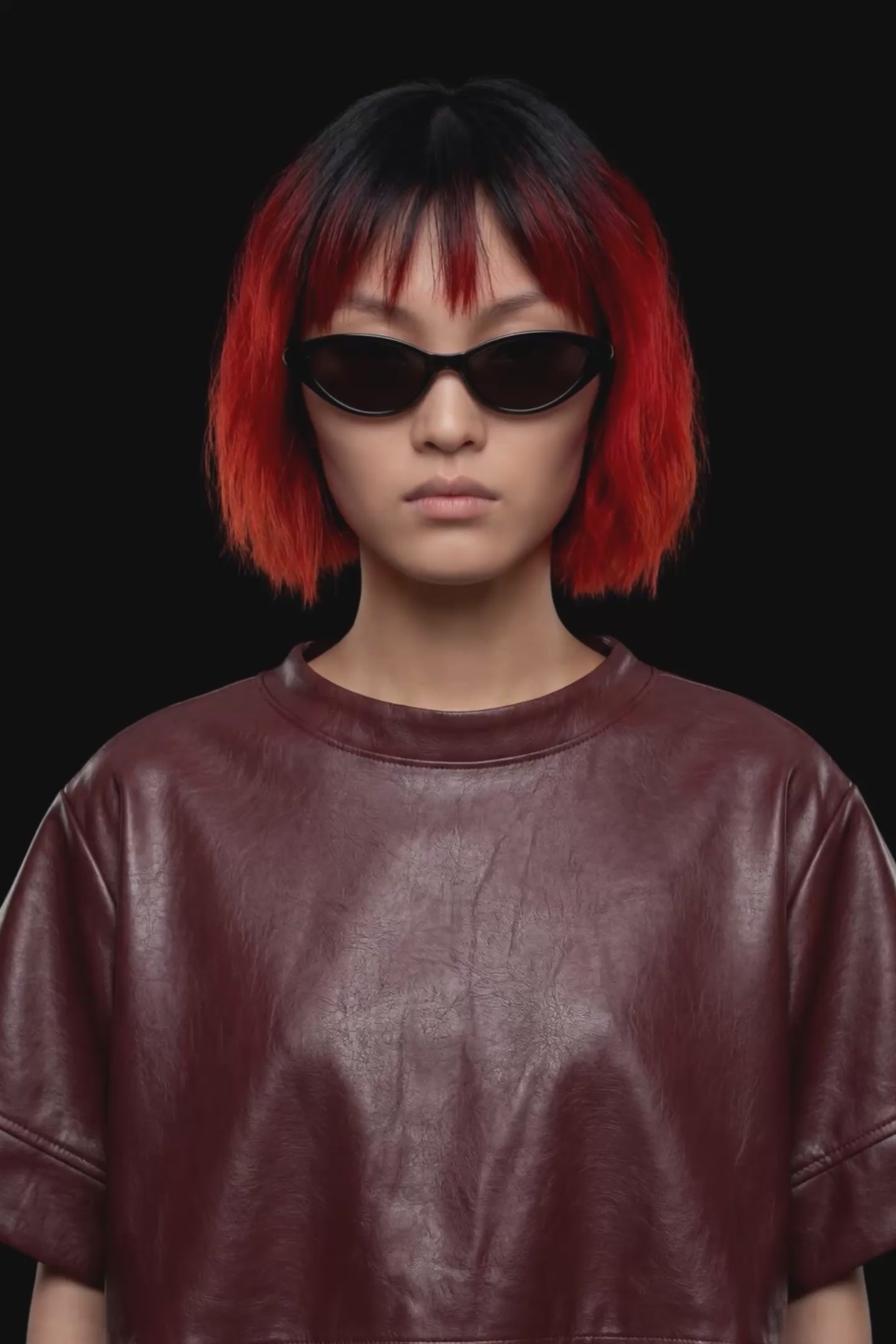 A short-sleeve cropped faux-leather top in a deep burgundy color, featuring a layered asymmetrical hem, displayed against a solid black background.
