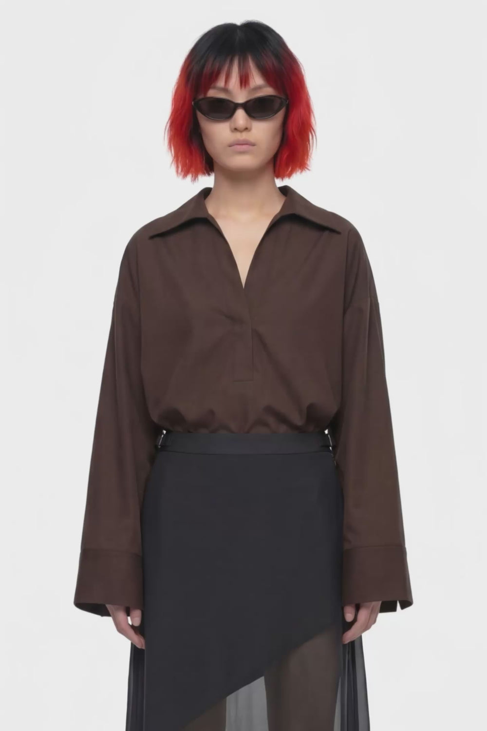 A black midi skirt with a structured waistband and an asymmetrical draped overlay, shown against a plain white background.