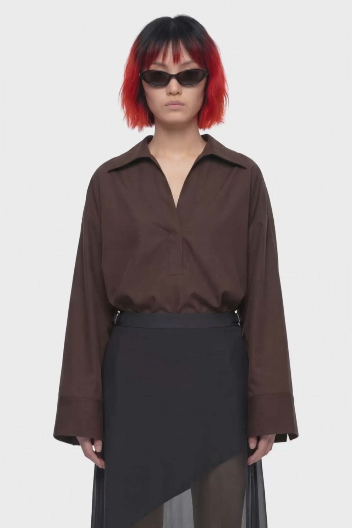 A black midi skirt with a structured waistband and an asymmetrical draped overlay, shown against a plain white background.