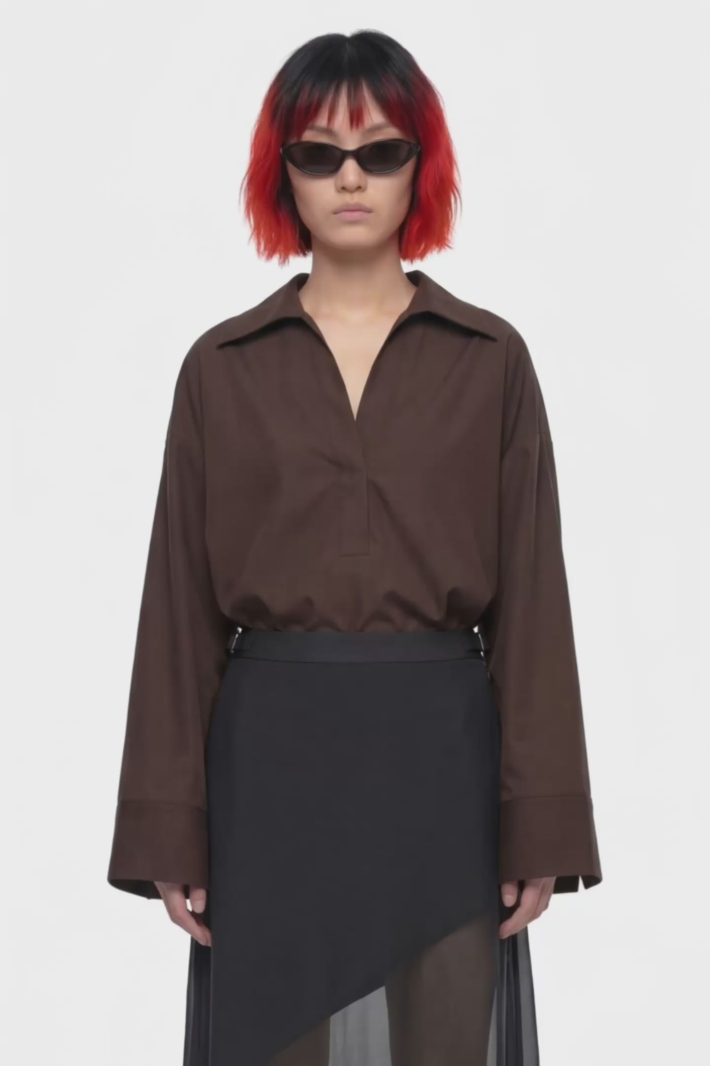A black midi skirt with a structured waistband and an asymmetrical draped overlay, shown against a plain white background.