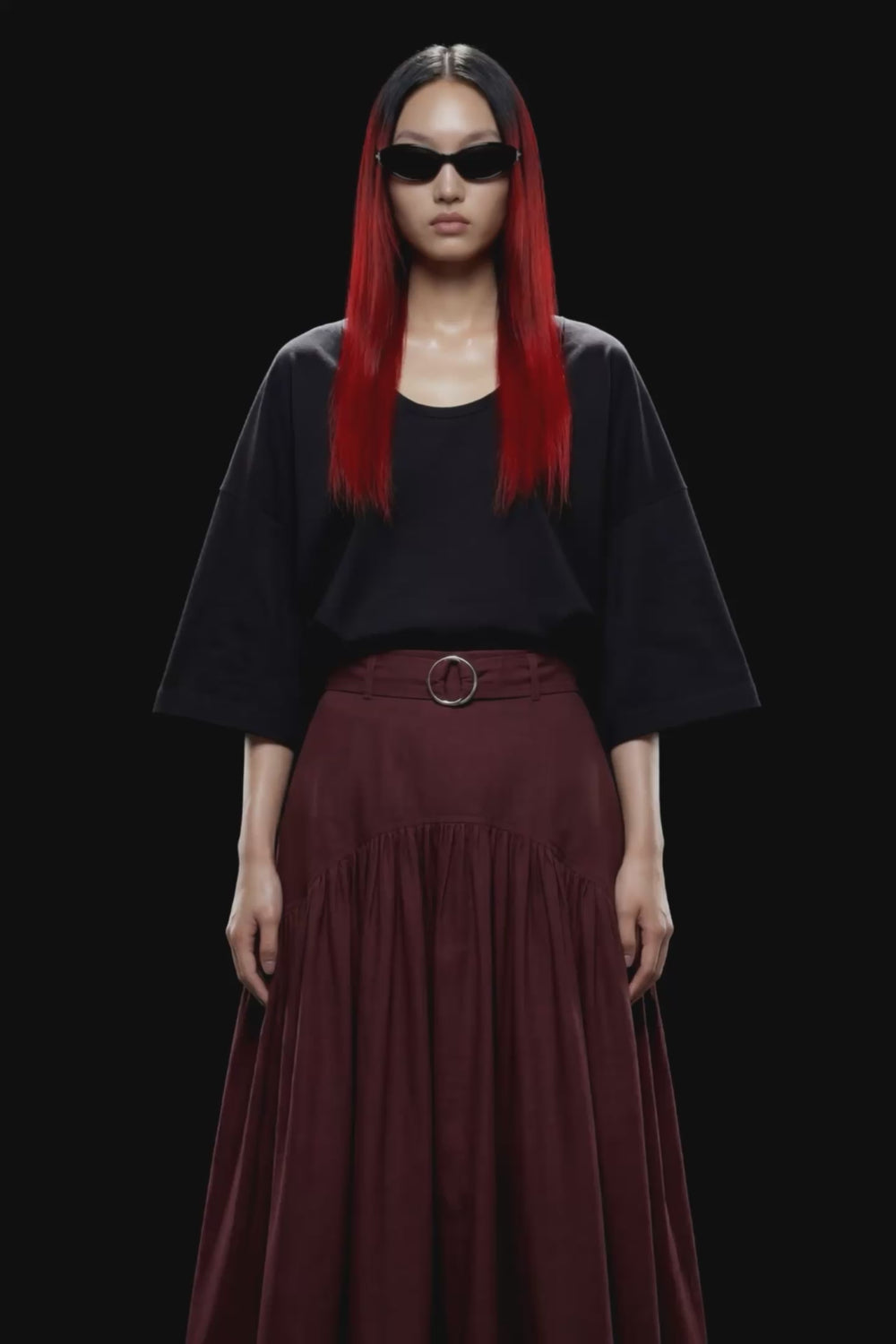 A dark burgundy pleated midi skirt with a matching waistband belt and silver-tone ring buckle, shown against a solid black background.