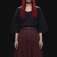 A dark burgundy pleated midi skirt with a matching waistband belt and silver-tone ring buckle, shown against a solid black background.