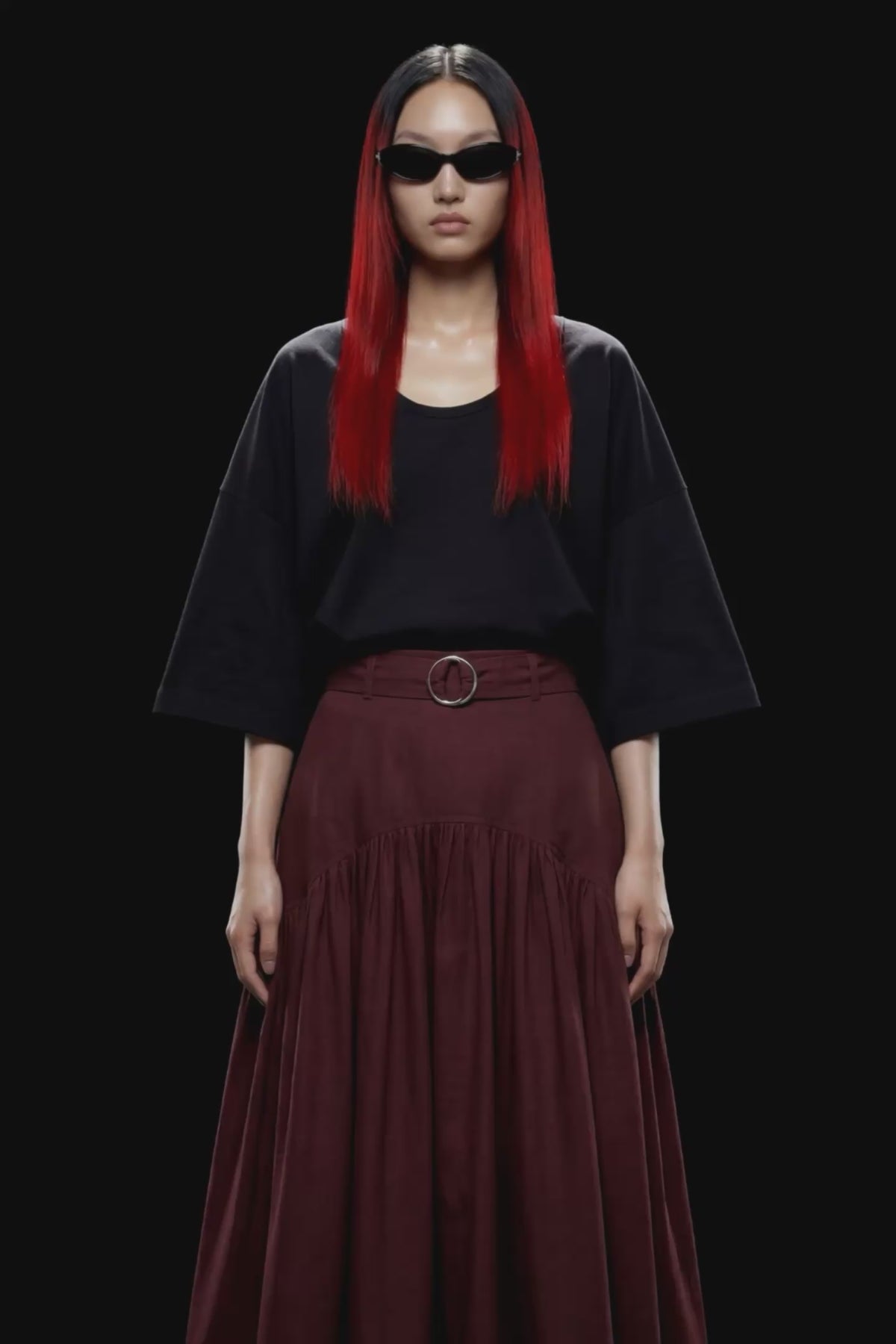 A dark burgundy pleated midi skirt with a matching waistband belt and silver-tone ring buckle, shown against a solid black background.