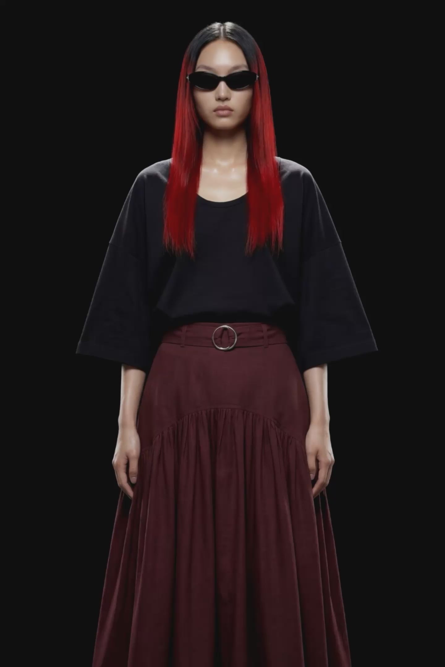 A dark burgundy pleated midi skirt with a matching waistband belt and silver-tone ring buckle, shown against a solid black background.