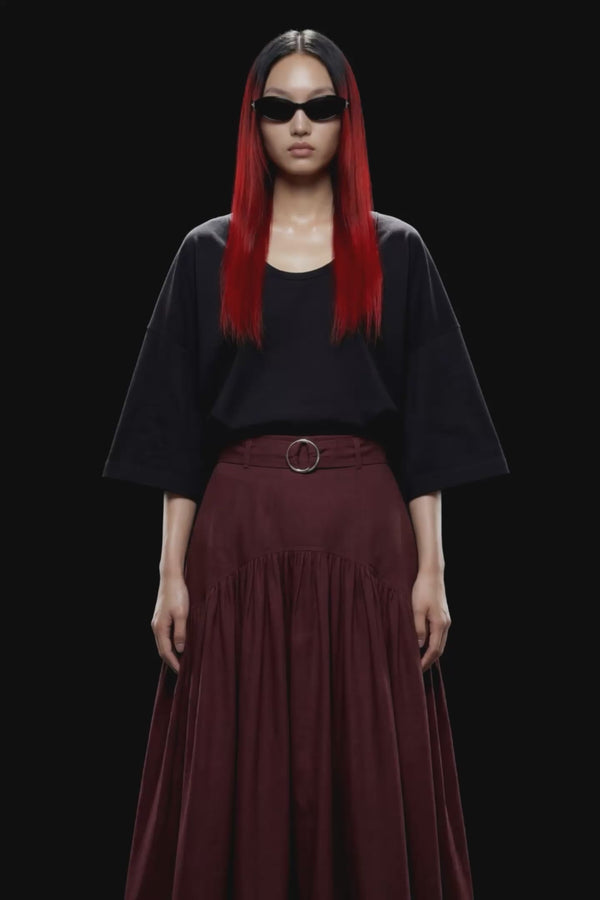 A dark burgundy pleated midi skirt with a matching waistband belt and silver-tone ring buckle, shown against a solid black background.