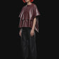 A short-sleeve cropped faux-leather top in a deep burgundy color, featuring a layered asymmetrical hem, displayed against a solid black background.
