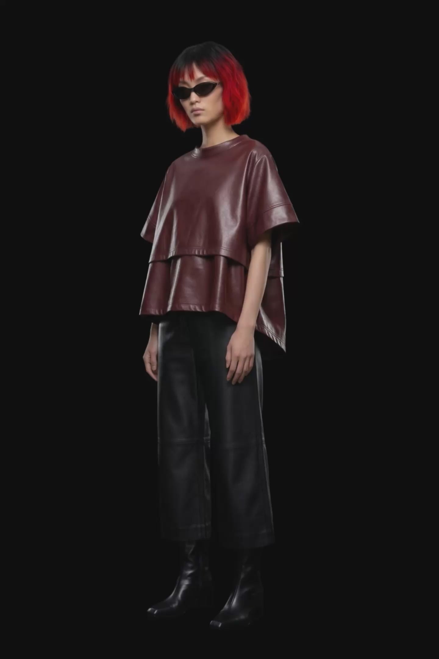 A short-sleeve cropped faux-leather top in a deep burgundy color, featuring a layered asymmetrical hem, displayed against a solid black background.