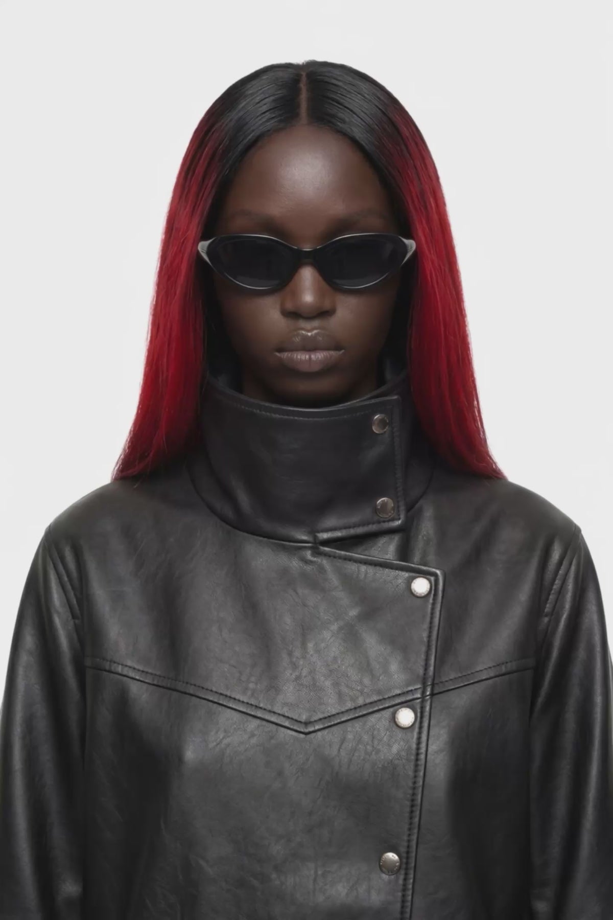A black leather jacket with a high mock neck, asymmetrical snap button closure, and ribbed sleeve detailing, shown against a plain white background.