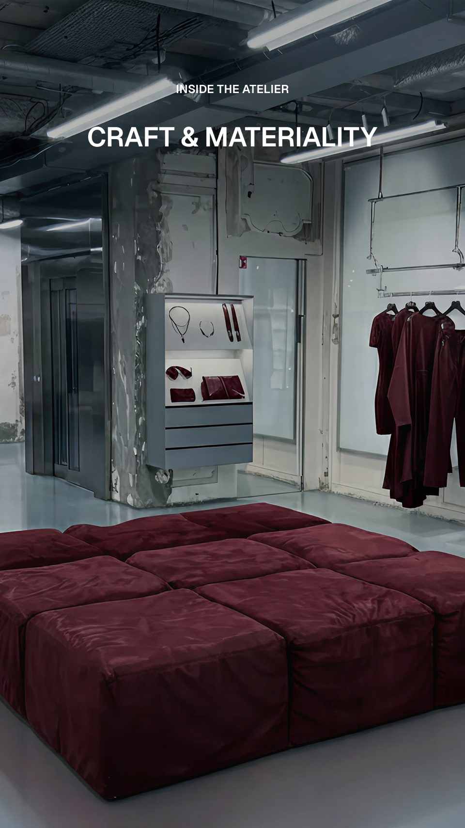 A large modular upholstered ottoman or lounge bed in deep burgundy is shown in a modern industrial atelier interior. White text at the top reads 'INSIDE THE ATELIER' and 'CRAFT & MATERIALITY'.