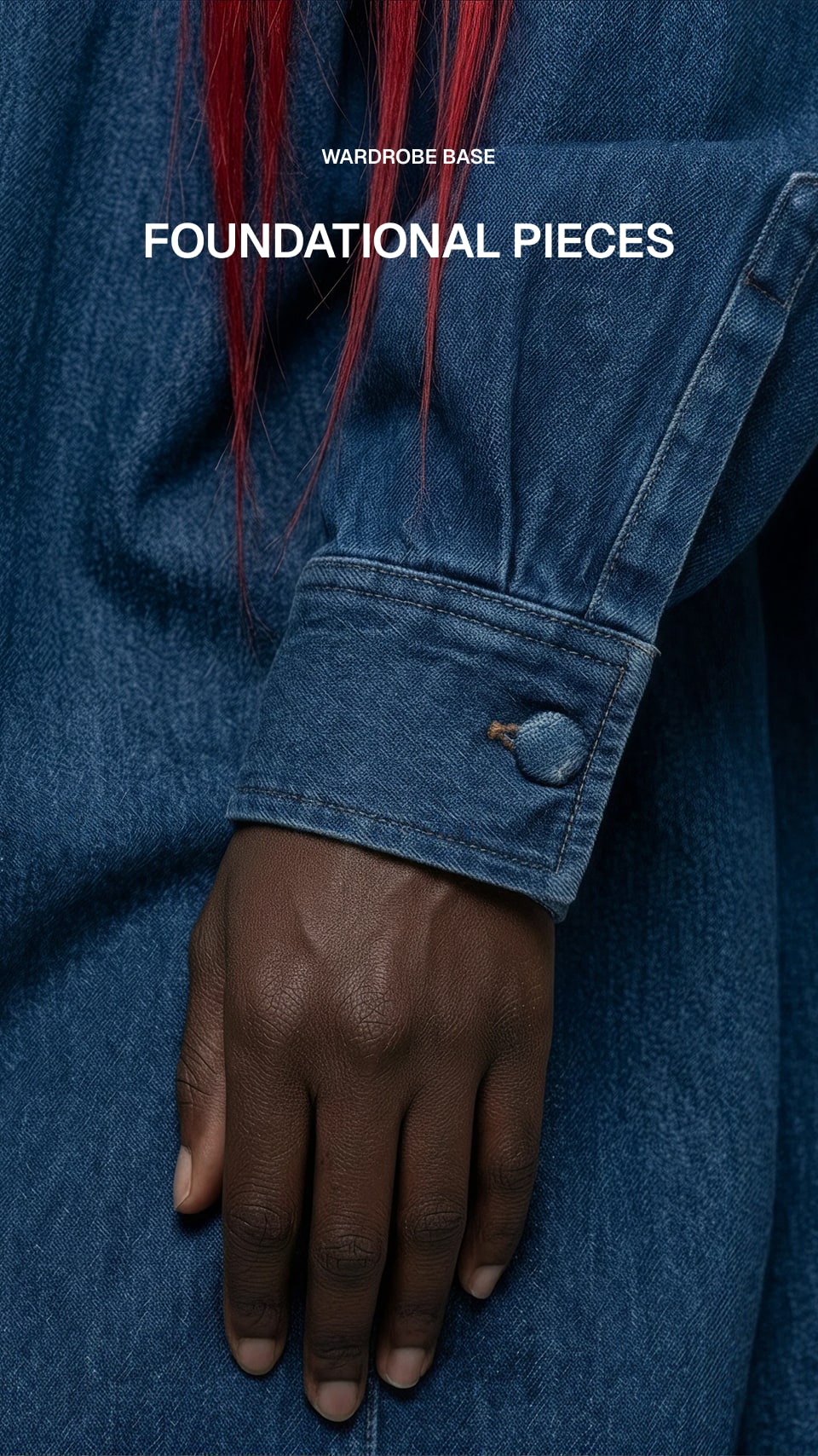 A close-up of a person wearing a blue denim jacket or shirt, showing the sleeve cuff with a button and a hand resting below it. Red hair is visible at the top, and white text at the top reads 'WARDROBE BASE' and 'FOUNDATIONAL PIECES'.
