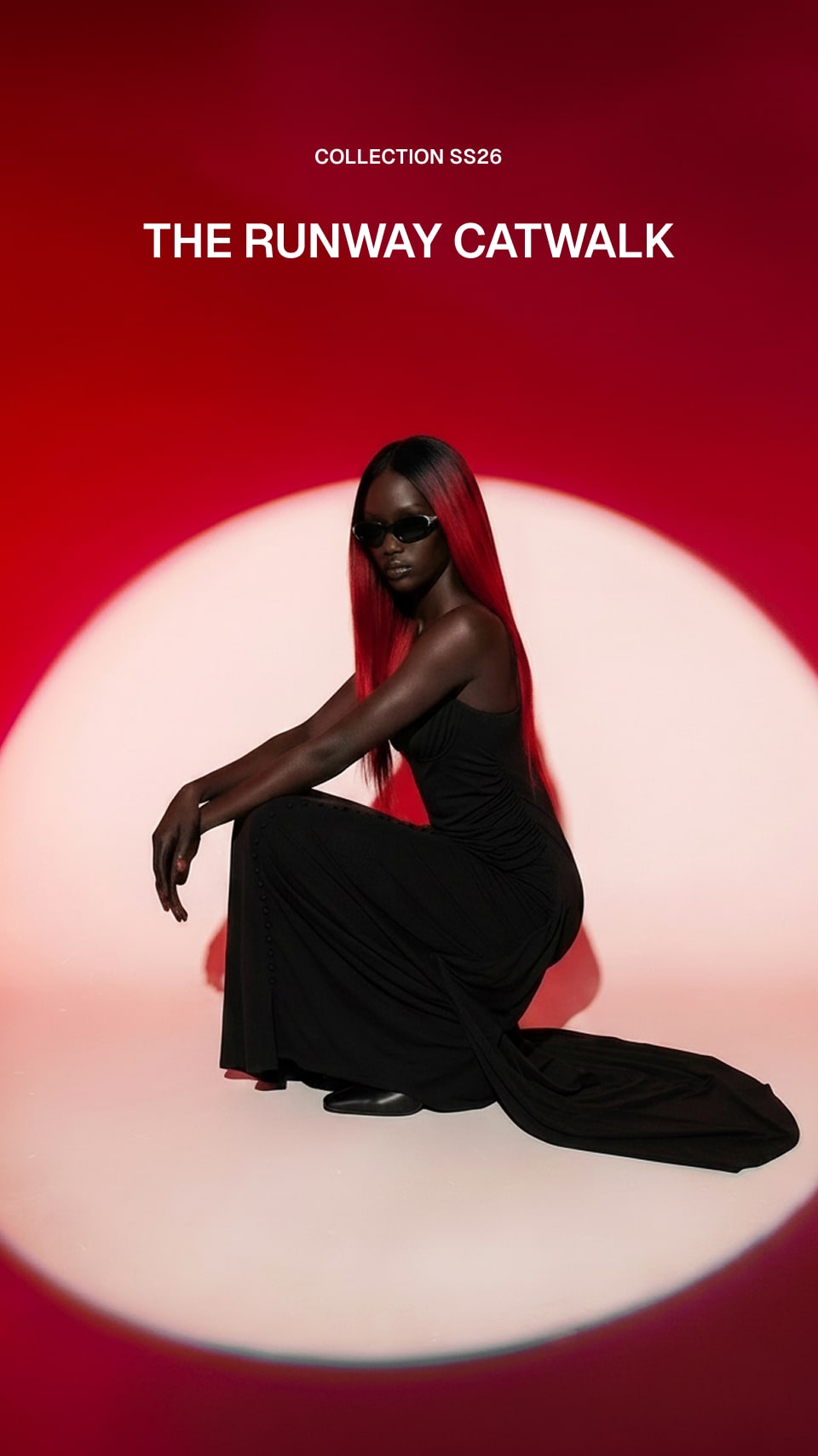 A model with long red hair and black sunglasses sits in a black gown on a circular white platform against a red background. White text at the top reads 'COLLECTION SS26 THE RUNWAY CATWALK'.